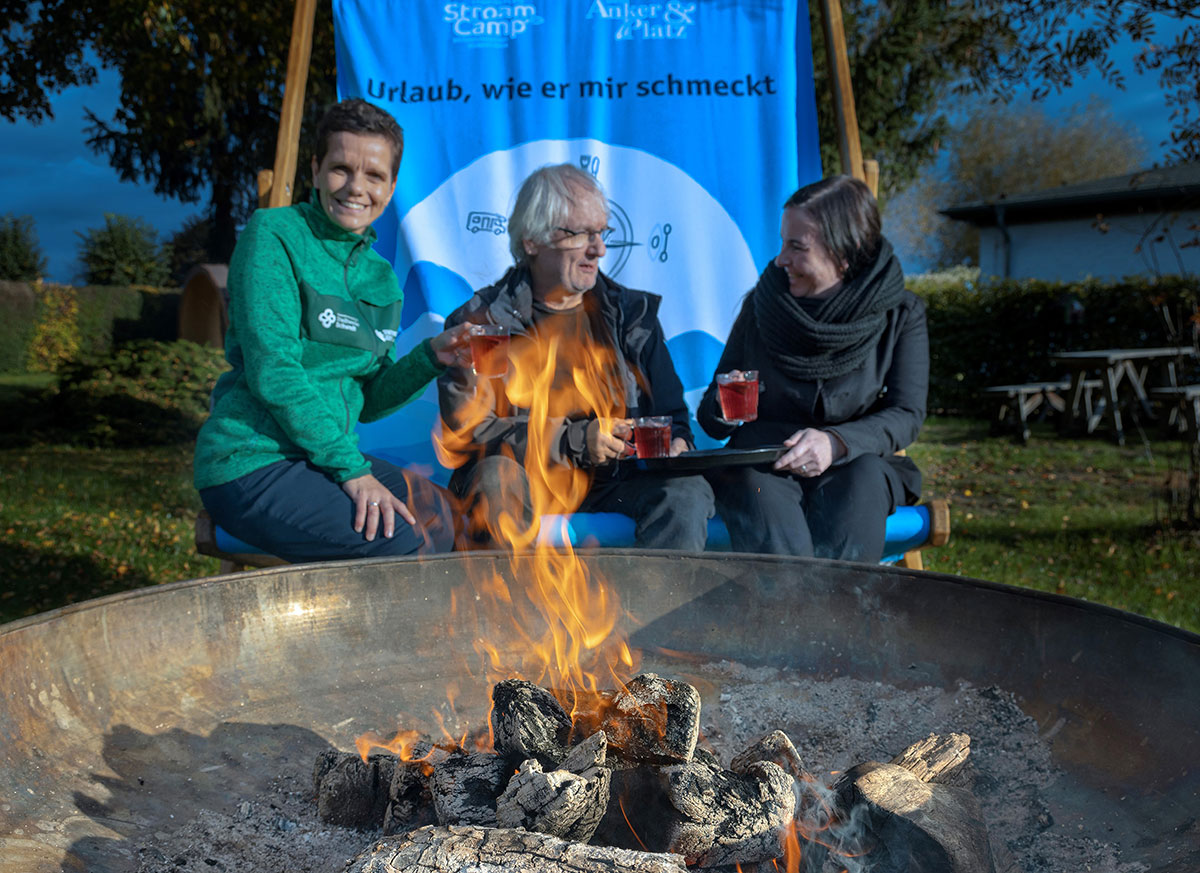 3 Personen sitzen mit heißem Tee an einer Feurerschale
